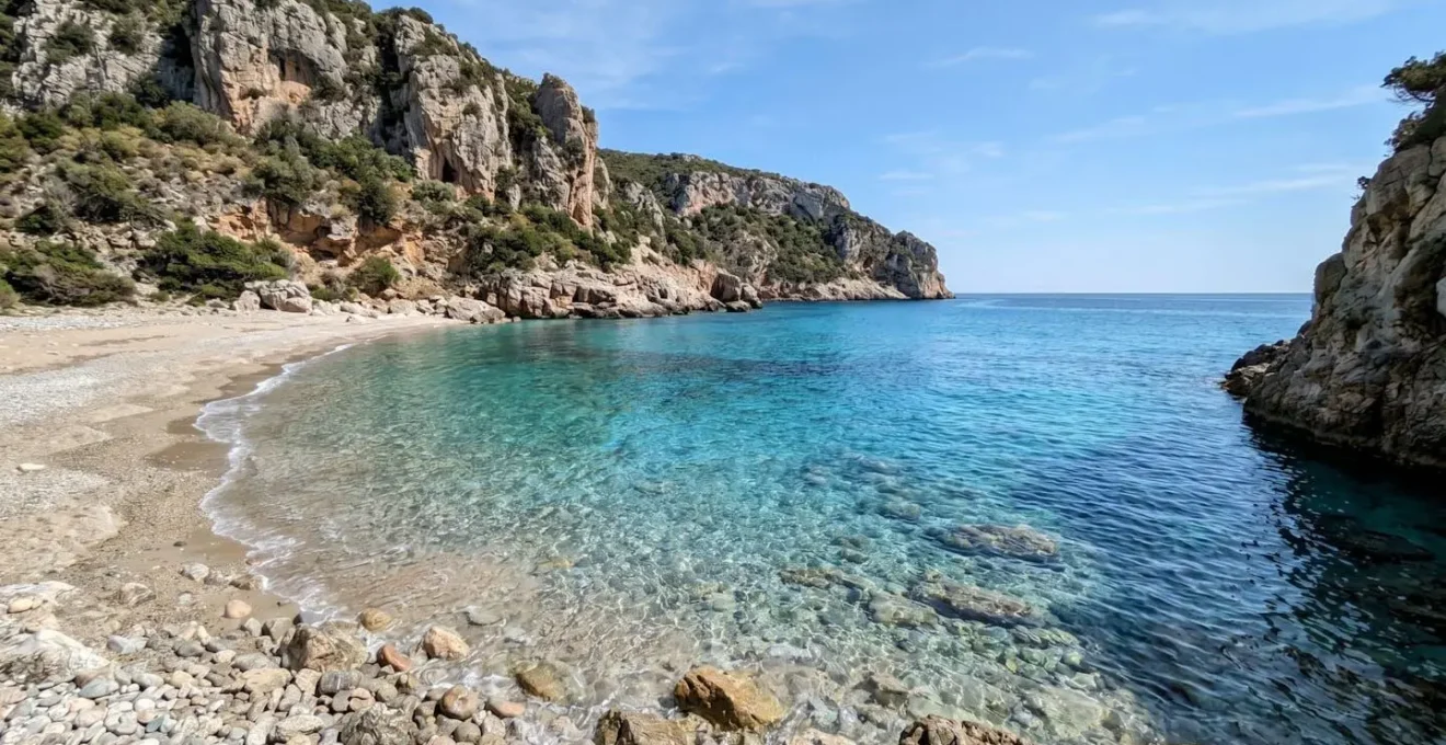 Una piccola caletta sarda con acqua cristallina turchese circondata da scogliere naturali, completamente deserta sotto la luce del sole