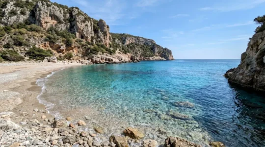 Una piccola caletta sarda con acqua cristallina turchese circondata da scogliere naturali, completamente deserta sotto la luce del sole