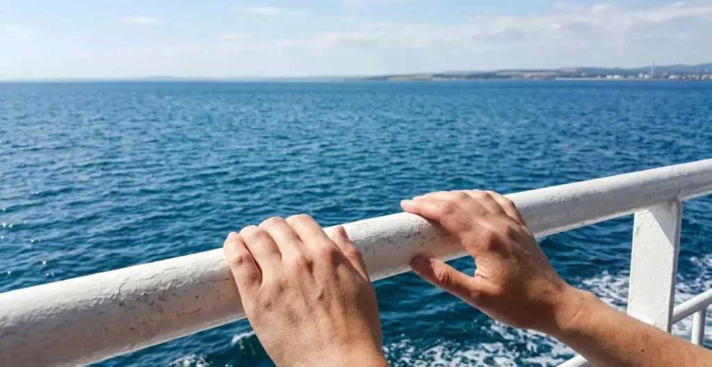 Primo piano di mani appoggiate alla ringhiera metallica di un traghetto con il mare azzurro completamente sfocato sullo sfondo Primo piano di mani appoggiate alla ringhiera metallica di un traghetto con il mare azzurro completamente sfocato sullo sfondo